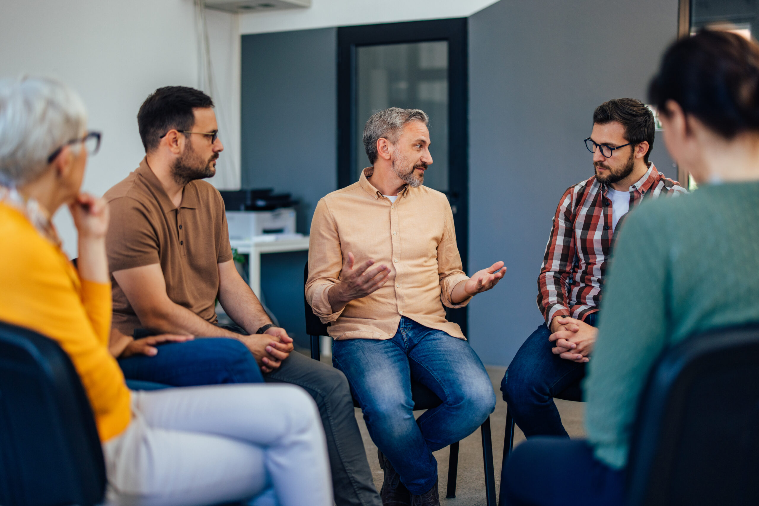 Three males sitting next to each other, talking to the others from the group therapy.