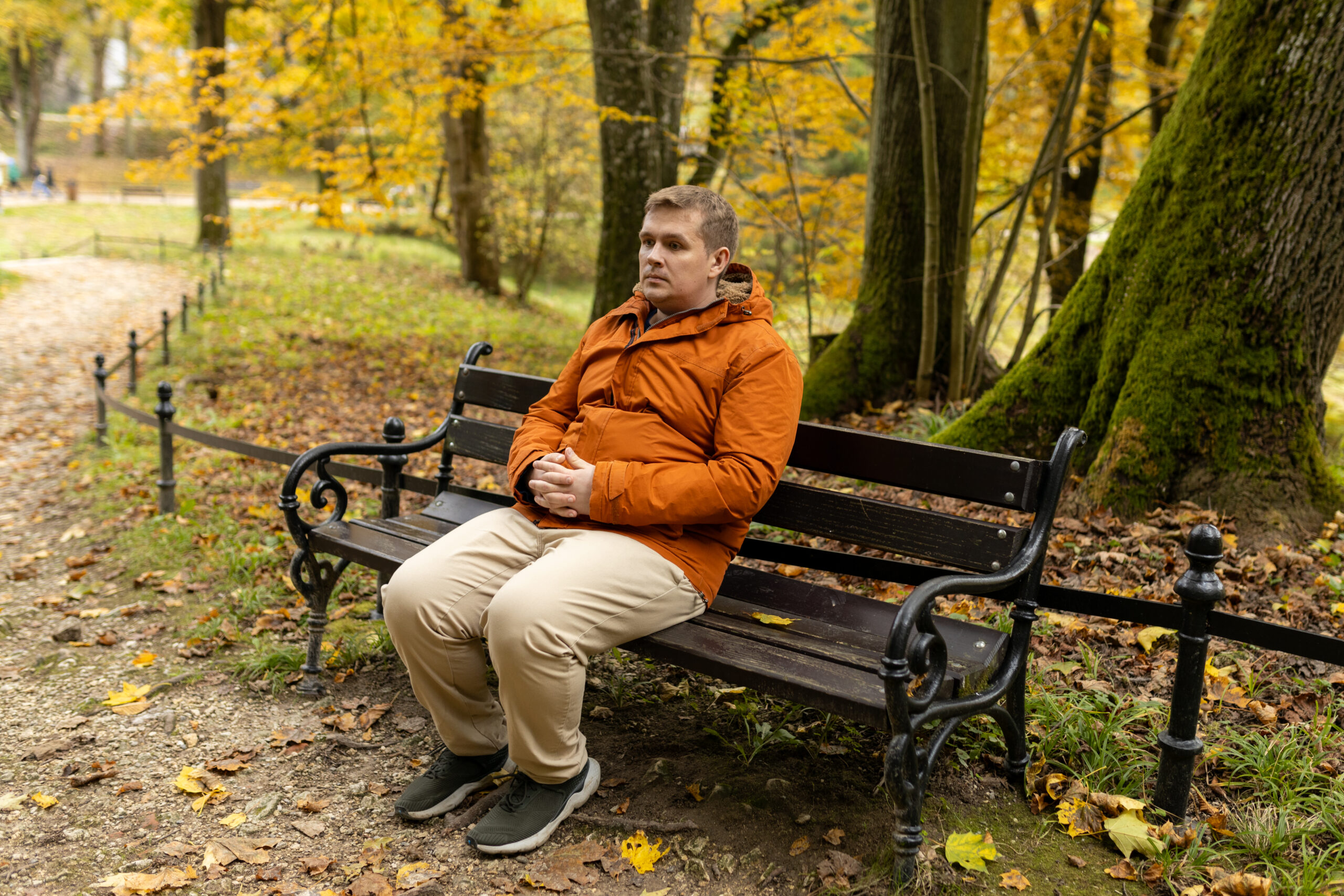 Young sad 30s man sitting alone on bench in autumn park. Thinking about life. Spending time alone in nature. Tired lost human guy wait, worship God